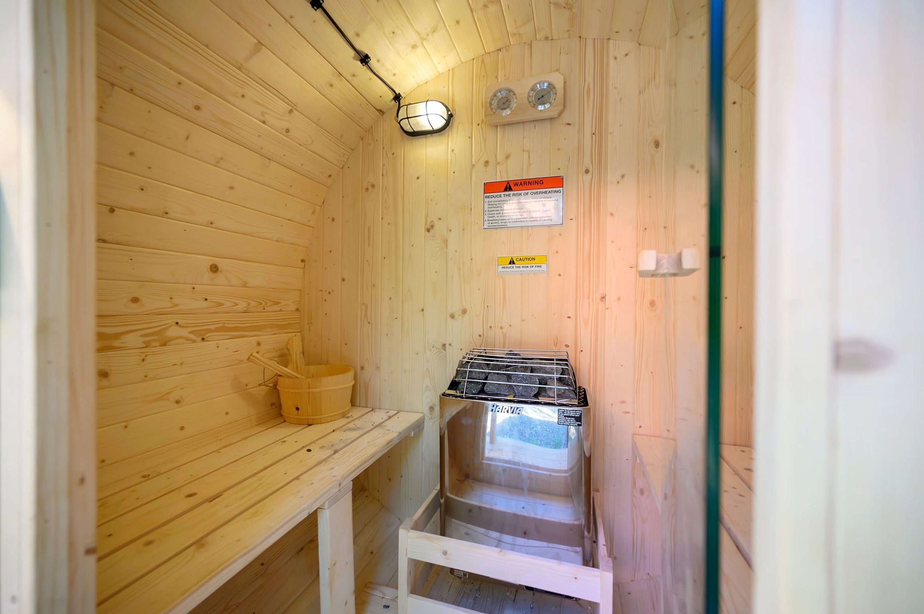 A sauna with wooden walls, a bench, a heater, and safety warning signs.