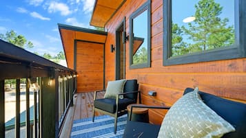 Een houten chalet met een terras, een bank met kussens, en een groot raam.
