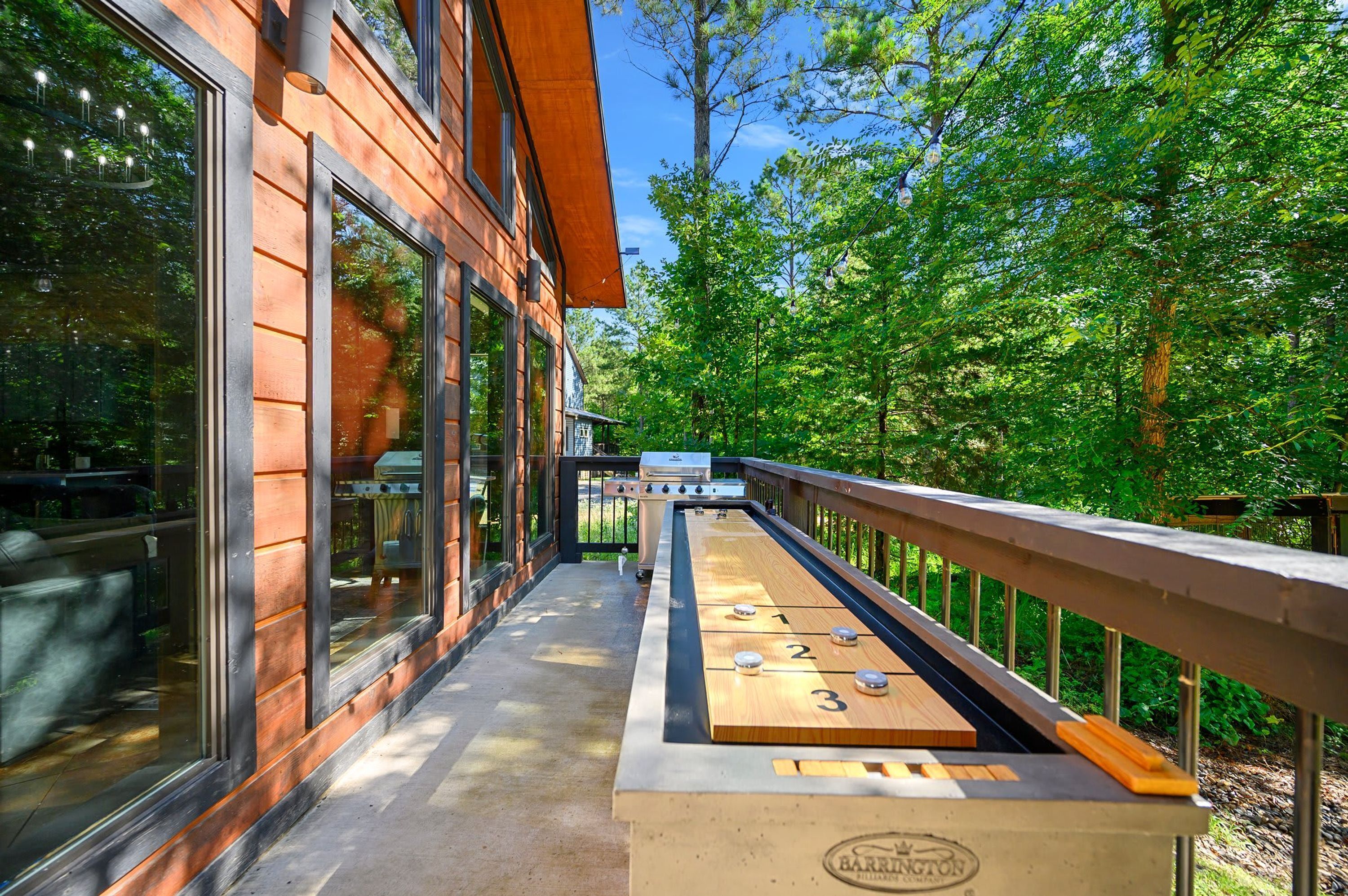 A wooden deck with a shuffleboard table, surrounded by glass windows and a wooden railing.