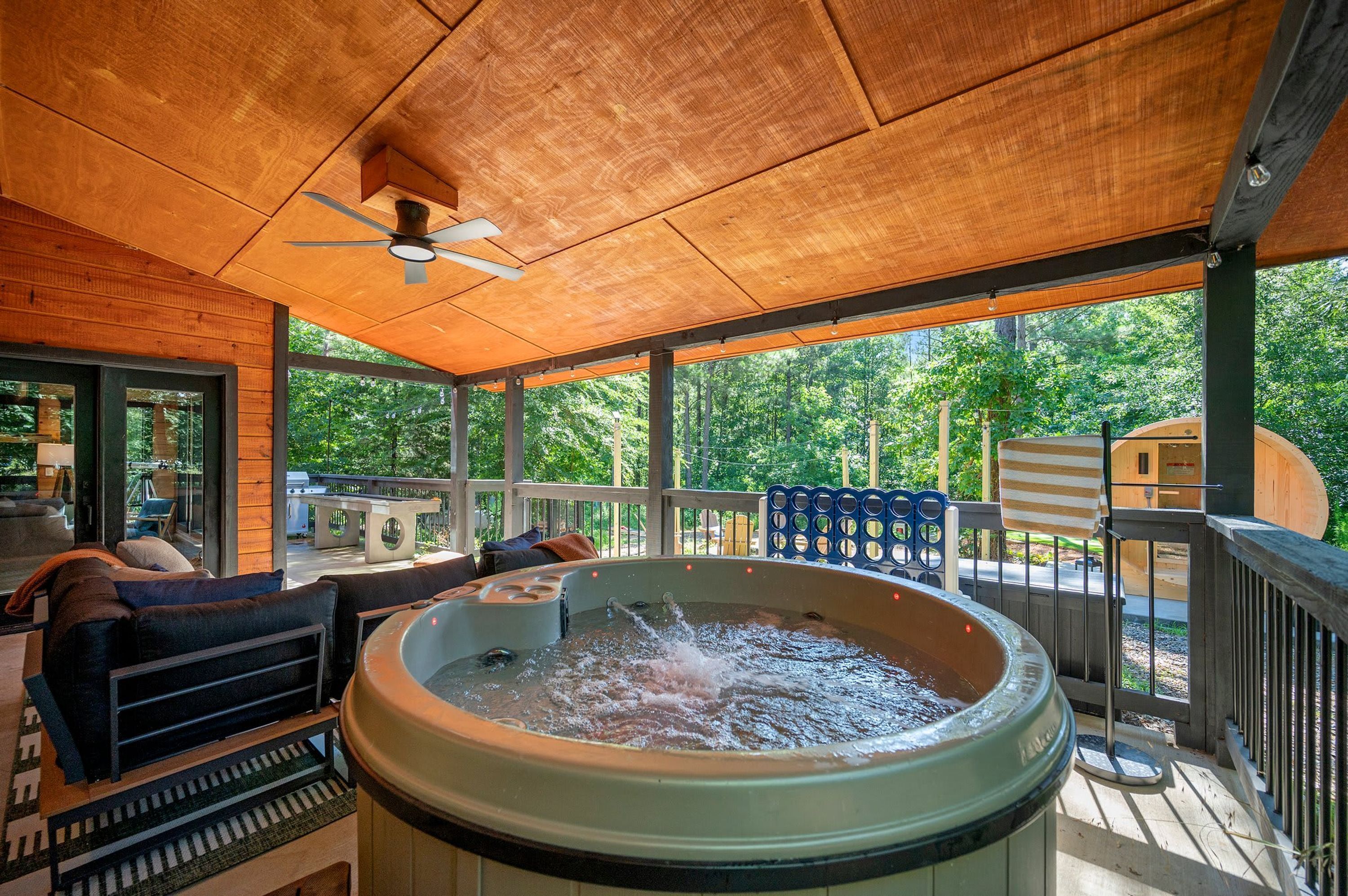 Un jacuzzi debajo de una terraza de madera, con mobiliario exterior y vistas al follaje circundante.