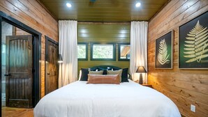 Een kamer met houten lambrisering, een groot bed, twee ramen en een deur.