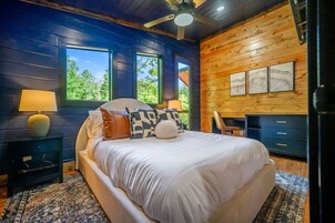 Un dormitorio con una cama grande, dos ventanas, un ventilador de techo y una pared de madera con obras de arte.