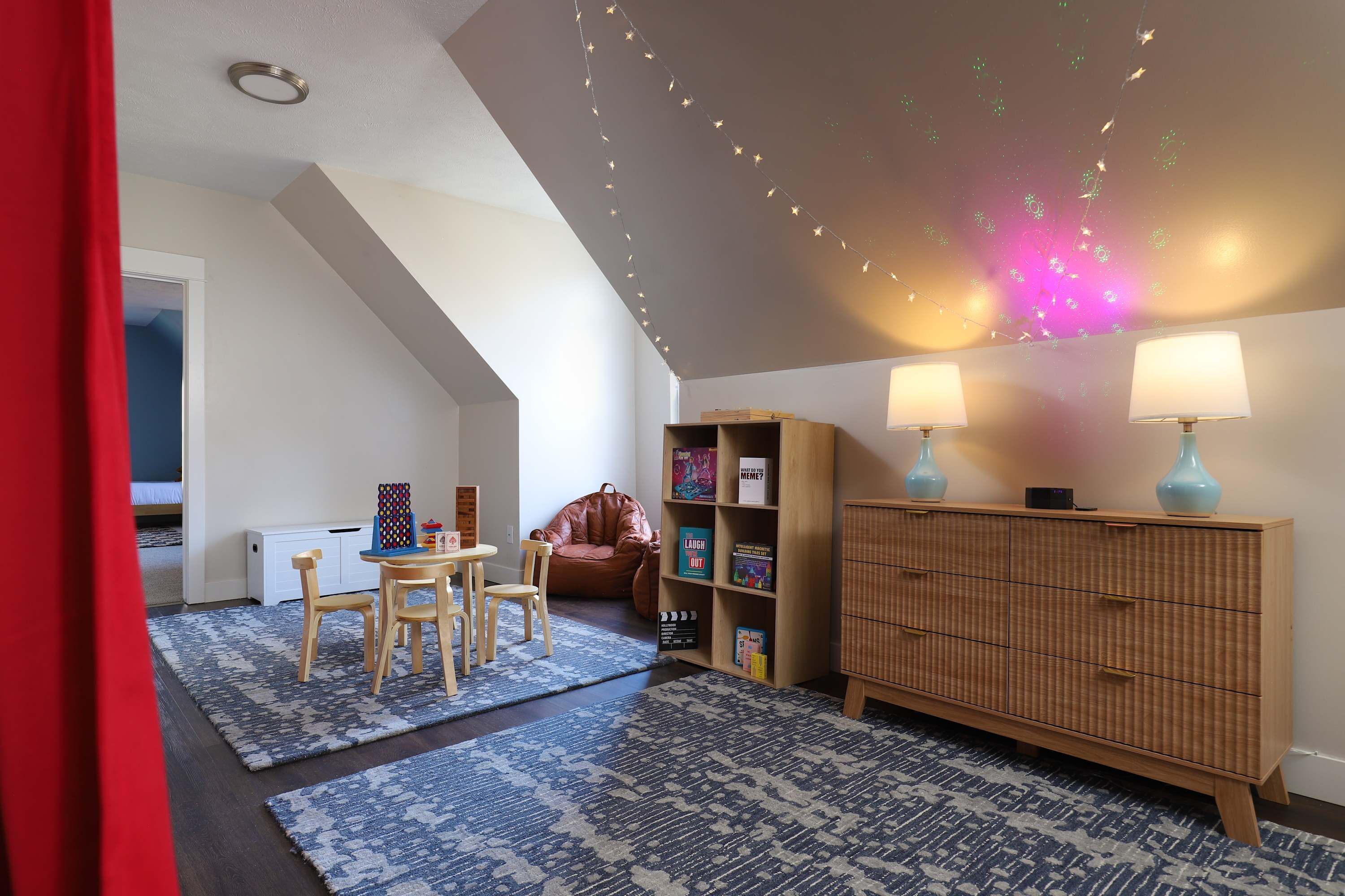 A cozy room with a sloped ceiling, a wooden cabinet, two lamps, a chair, and a small table.