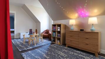 A cozy room with a sloped ceiling, a wooden cabinet, two lamps, a chair, and a small table.