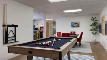 A pool table with balls, a billiard rack, and a nearby seating area with a table and chairs.