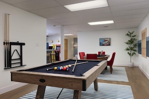 A pool table with balls, a billiard rack, and a nearby seating area with a table and chairs. - Pine Paddle Getaway Game Room Hot Tub Pool (Muskegon)