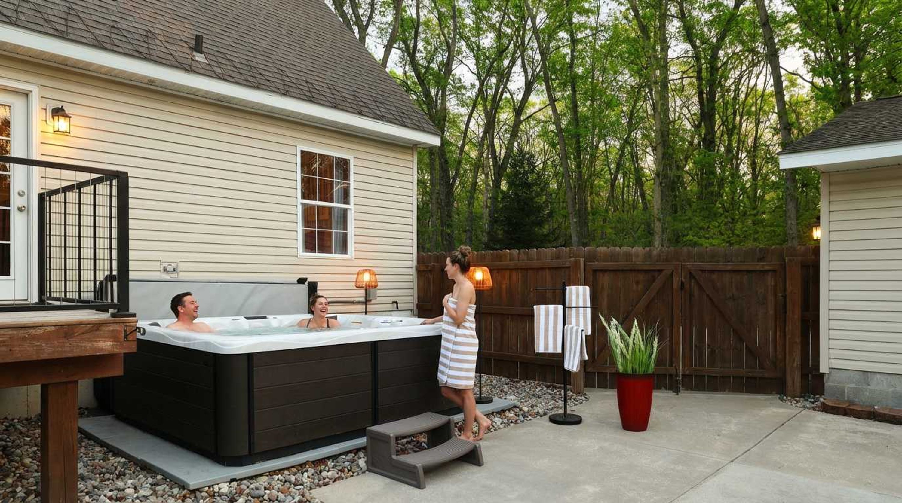 Un espace extérieur aménagé avec un jacuzzi, une terrasse en bois, une clôture en bois et un pot de fleurs.