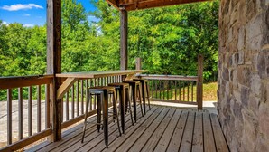 Una terraza de madera con barandilla, un muro de piedra y vistas a vegetación exuberante.