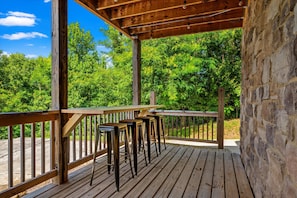 Eine Holzterrasse mit Geländer, eine Steinmauer und Blick auf üppiges Grün.