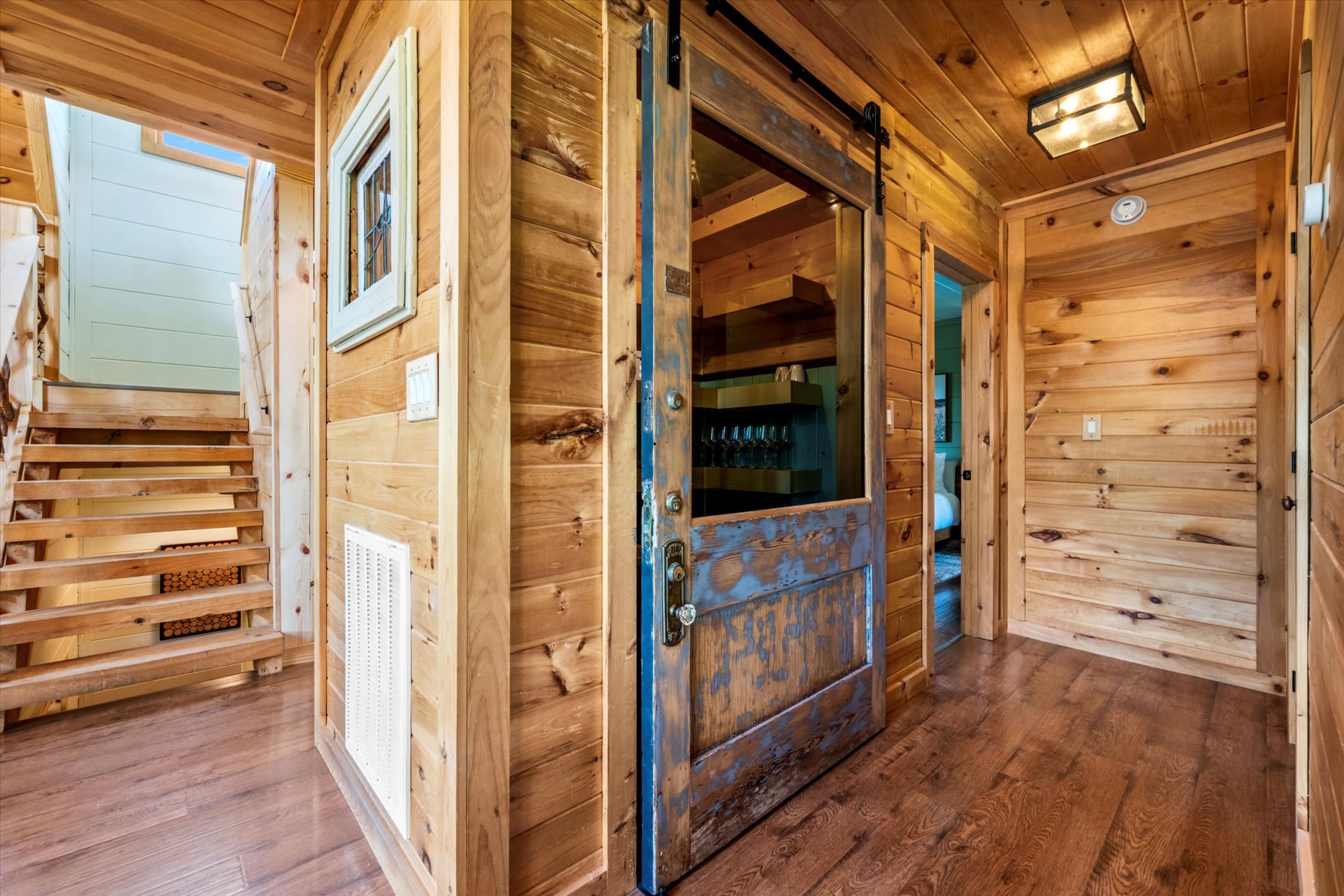 Interior de madera con un amplio portón corredero, una escalera y un ventanal visible.