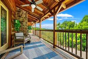 Una terraza de madera con un muro de piedra, un ventilador de techo y vistas al verdor.