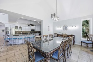 A modern kitchen with white cabinetry, a dining area with a glass table and wooden chairs, and a ceiling fan. - Coastal Luxe Retreat - Heated Pool - Games - Games (Hilton Head Island)
