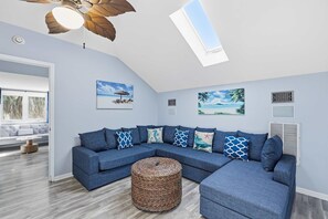 A modern living room with a sectional sofa, a round woven ottoman, and a ceiling fan. - Coastal Luxe Retreat - Heated Pool - Games - Games (Hilton Head Island)