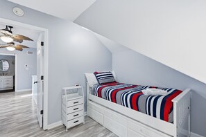 A bedroom with a sloped ceiling, a bed with a striped bedspread, a bedside table, and a wardrobe. - Coastal Luxe Retreat - Heated Pool - Games - Games (Hilton Head Island)