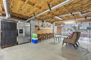 A kitchen with a refrigerator, bar stools, and a wicker chair. - Coastal Luxe Retreat - Heated Pool - Games - Games (Hilton Head Island)