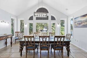 A dining area with a high ceiling, large windows, and a view of a house. - Coastal Luxe Retreat - Heated Pool - Games - Games (Hilton Head Island)
