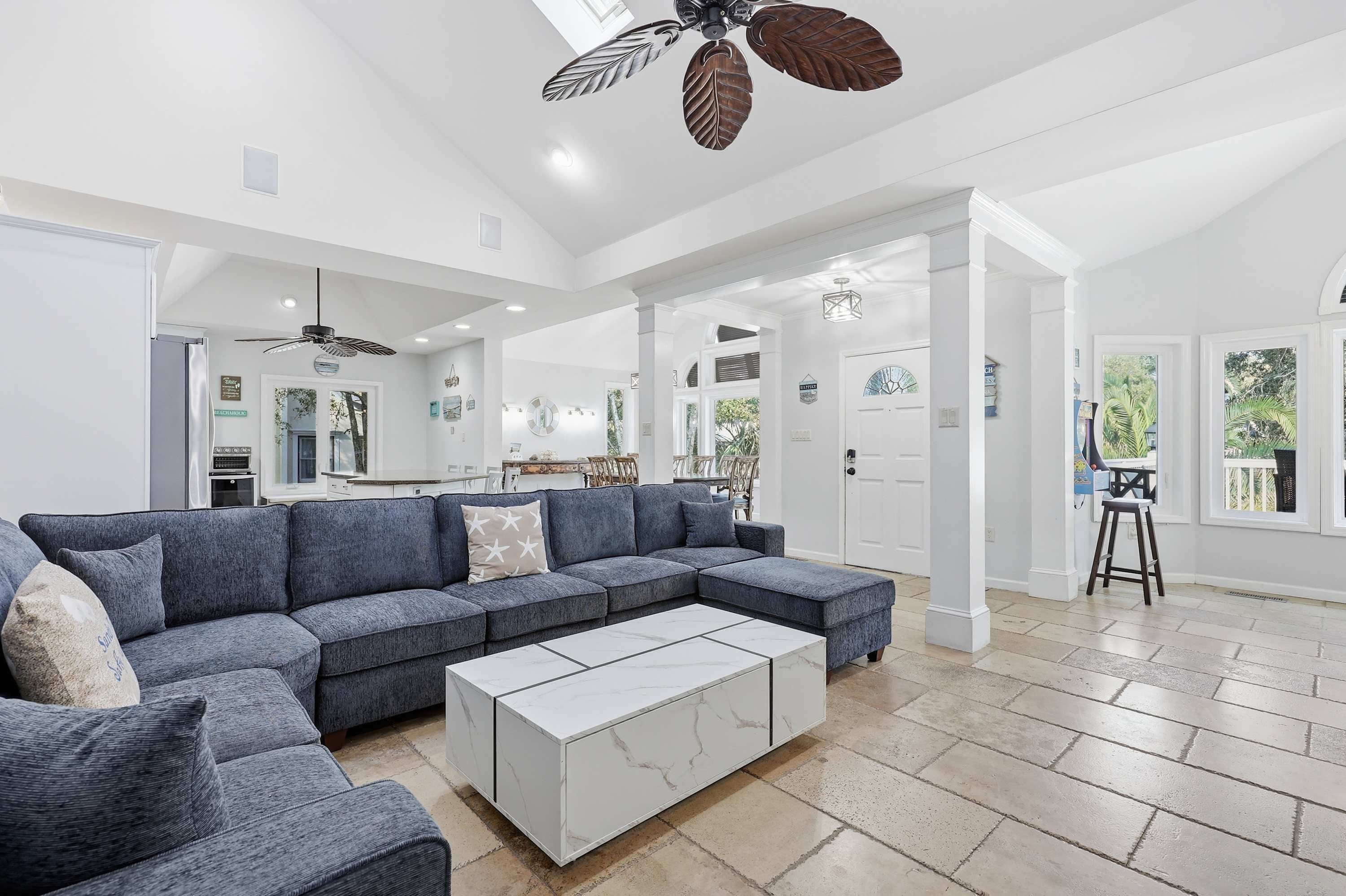 A spacious living room with a sectional sofa, a marble coffee table, and a ceiling fan with leaf designs.