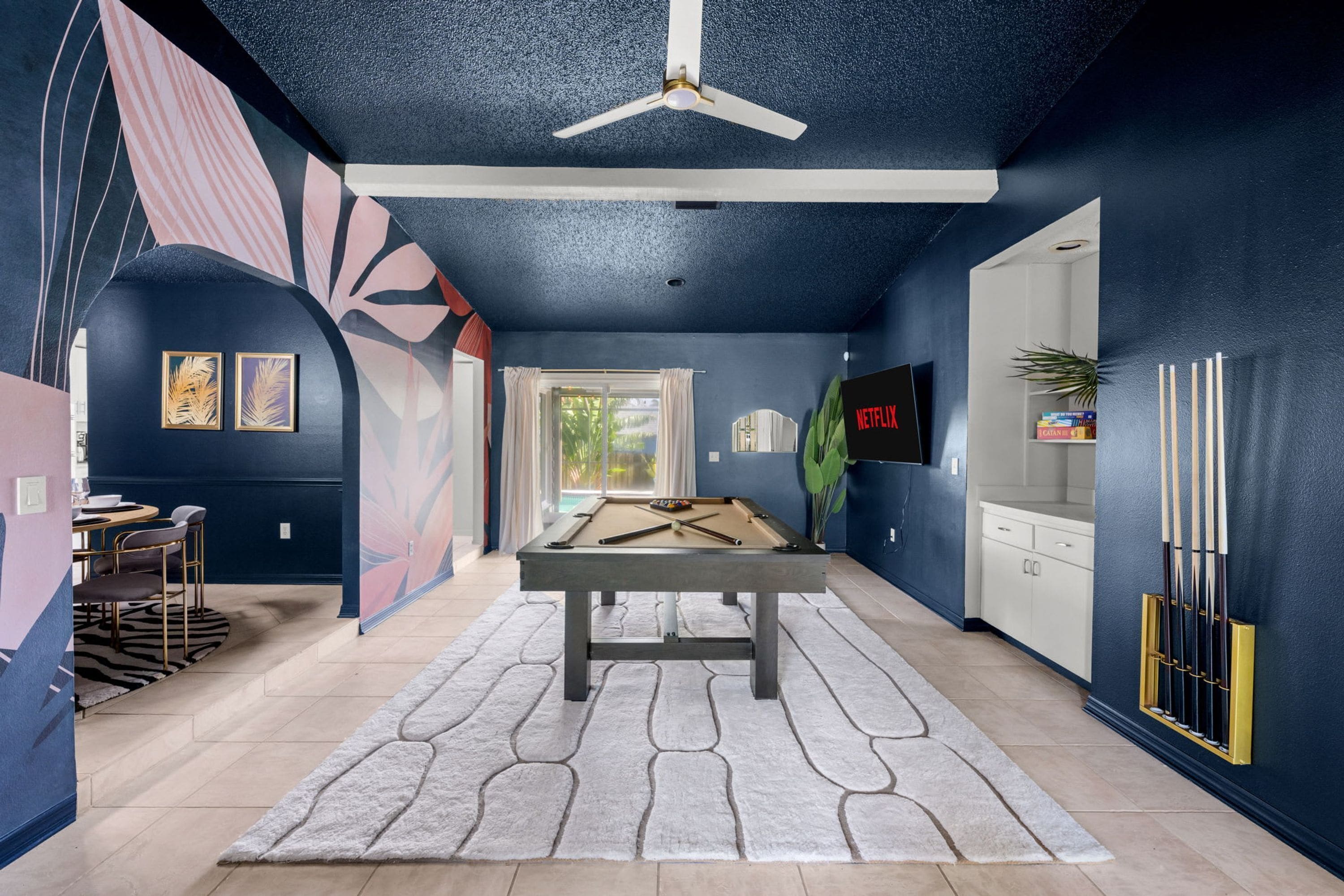Une pièce équipée d’une table de billard, d’un ventilateur de plafond et d’un téléviseur fixé au mur.