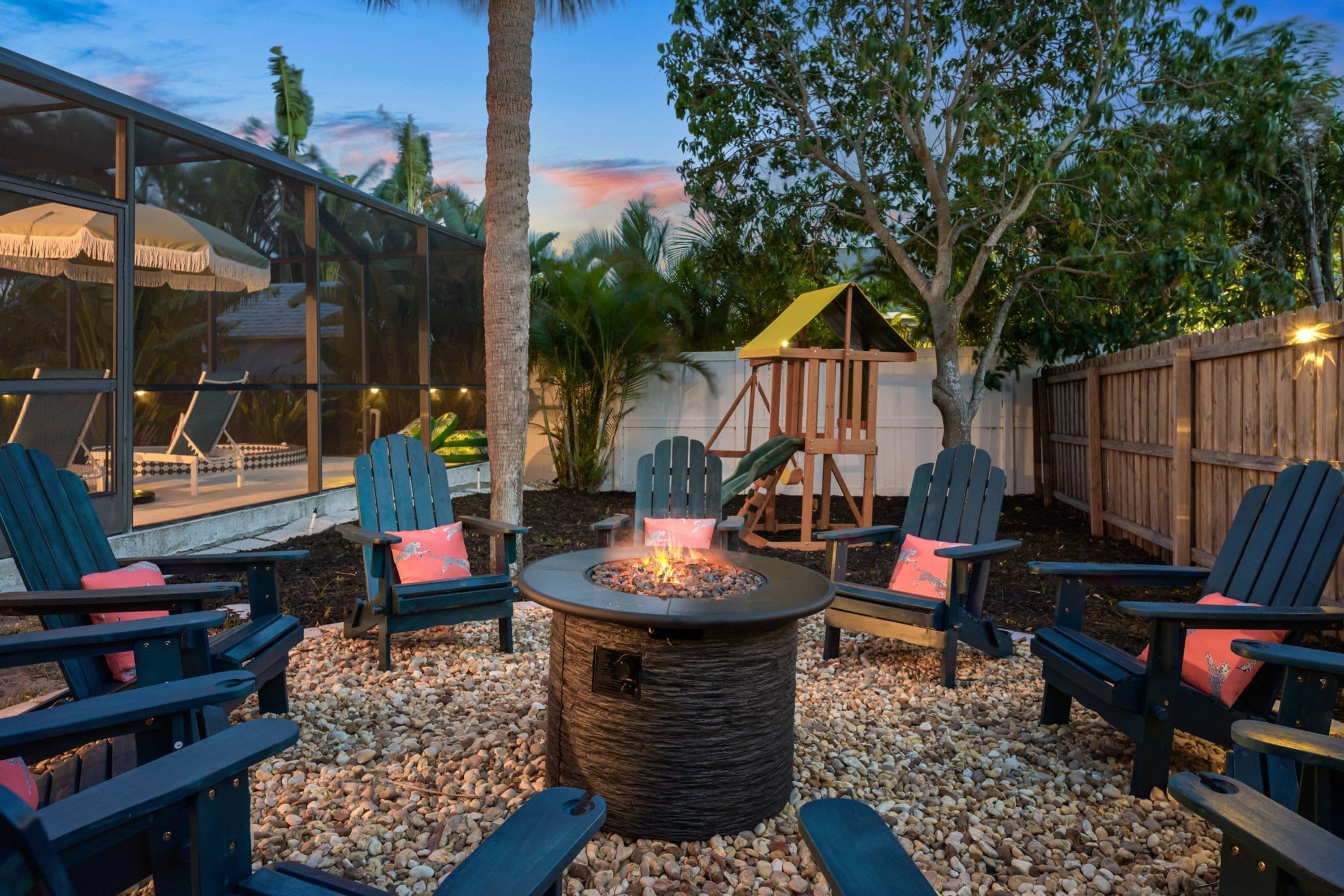 Un espacio de patio con sillas Adirondack, un pozo de fuego y una estructura de juegos de madera.