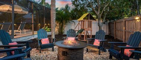 Un espacio de patio con sillas Adirondack, un pozo de fuego y una estructura de juegos de madera.
