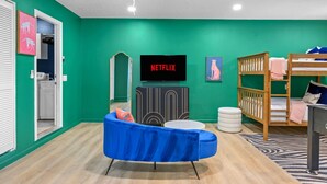 Ein Zimmer mit grüner Wand, blauem Sofa, Etagenbett, Fernseher und Schrank.