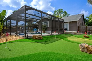 A house with a large glass enclosure, a well-maintained lawn, and a wooden fence. - Family Retreat Pool Putt Putt Playground (Bradenton)