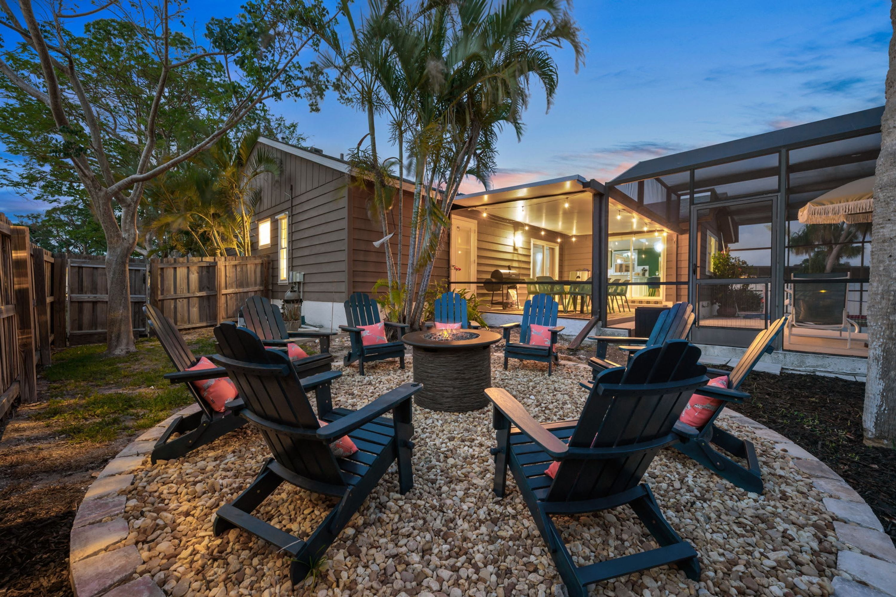 An outdoor seating area with Adirondack chairs and a fire pit, surrounded by a wooden deck and a stone border.