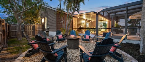 An outdoor seating area with Adirondack chairs and a fire pit, surrounded by a wooden deck and a stone border.