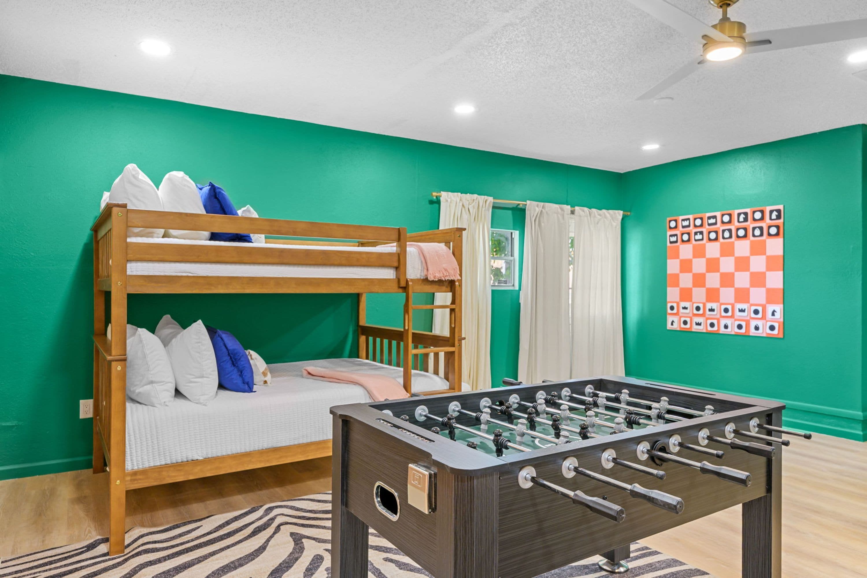 A room with a bunk bed, a foosball table, and a chessboard on the wall.