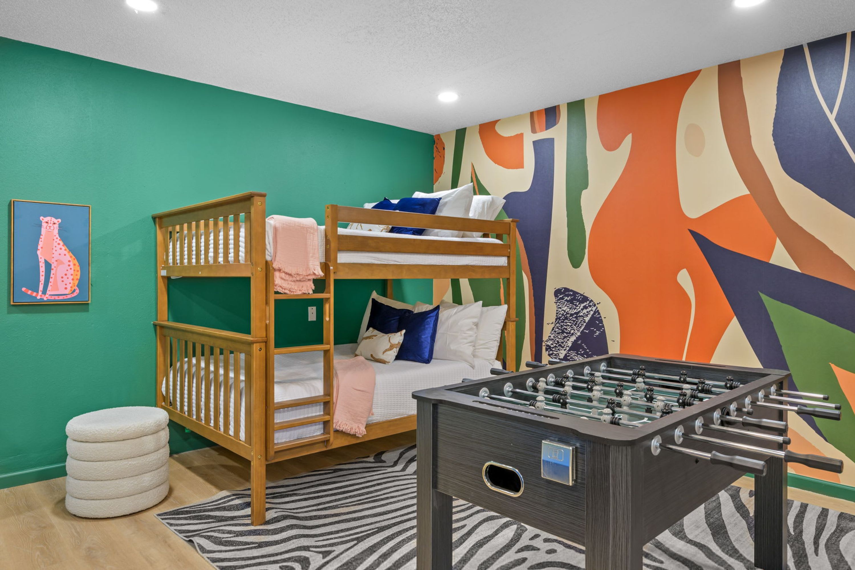 A room with bunk beds, a foosball table, and a colorful abstract wall mural.