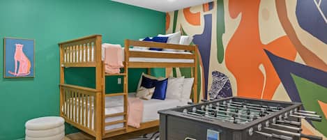 A room with bunk beds, a foosball table, and a colorful abstract wall mural.