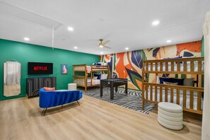 A room with a bunk bed, a foosball table, a blue sofa, a foosball table, a television, and a wall with a colorful abstract design. - Family Retreat Pool Putt Putt Playground (Bradenton)