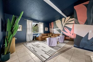 A living room with a sofa, two side tables, a large potted plant, and a patterned rug. - Family Retreat Pool Putt Putt Playground (Bradenton)