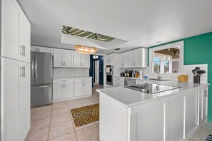 A modern kitchen with white cabinetry, a central island, and a unique ceiling design. - Family Retreat Pool Putt Putt Playground (Bradenton)