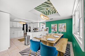 A modern kitchen with white cabinets, a central island, and a dining area with a wooden table and blue chairs. - Family Retreat Pool Putt Putt Playground (Bradenton)