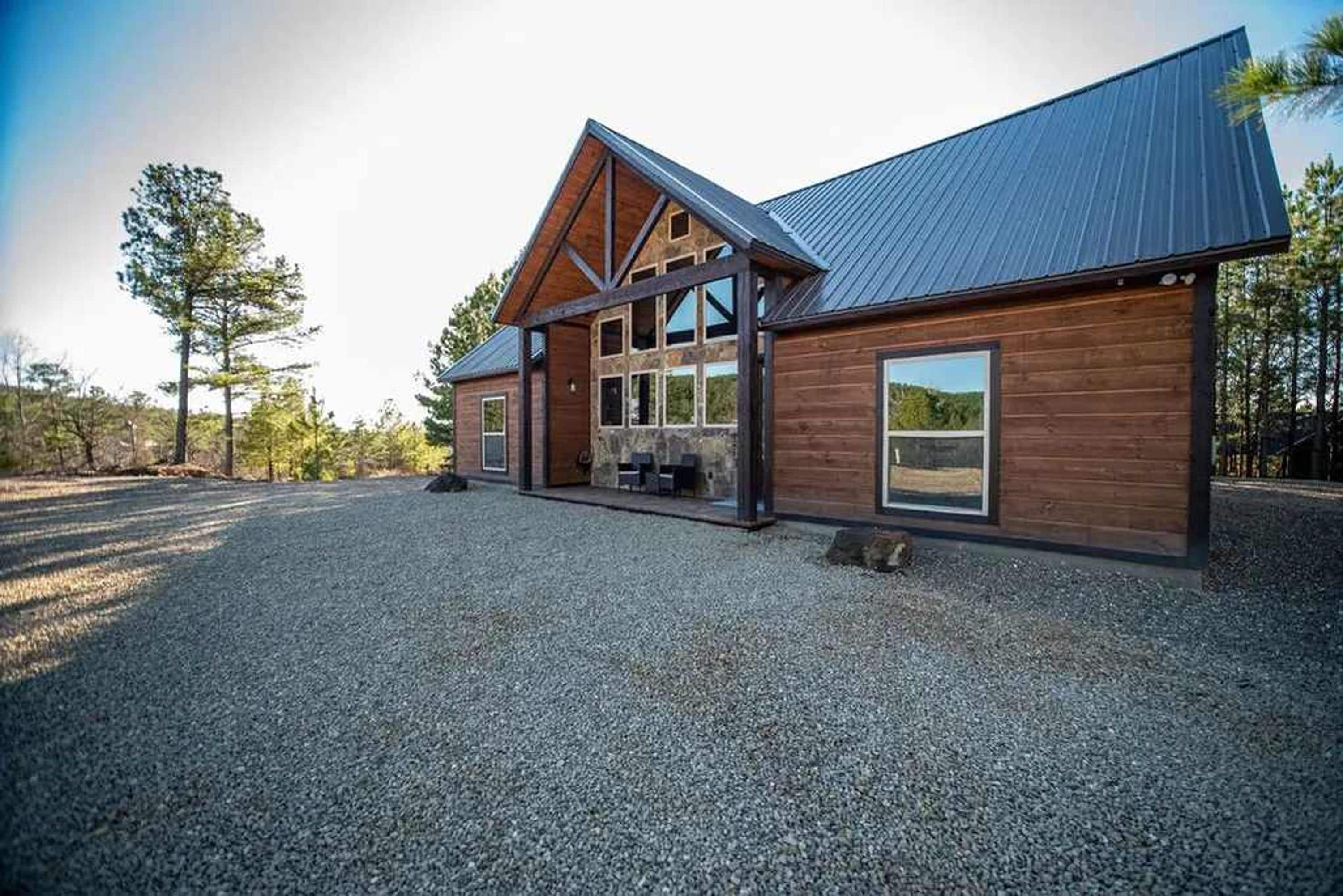 A two-story wooden building with a sloped roof, large windows, and a gravel driveway.