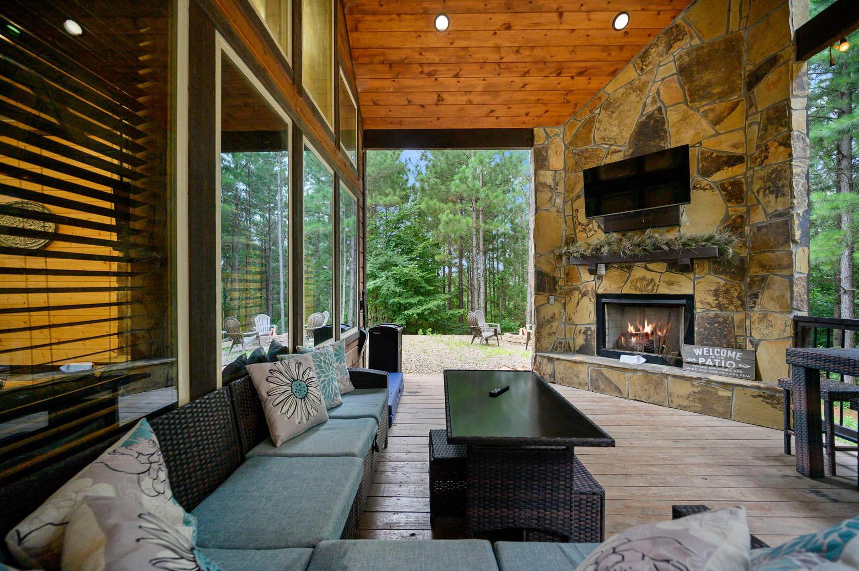 A covered outdoor seating area with a stone fireplace, a sofa, and a table.