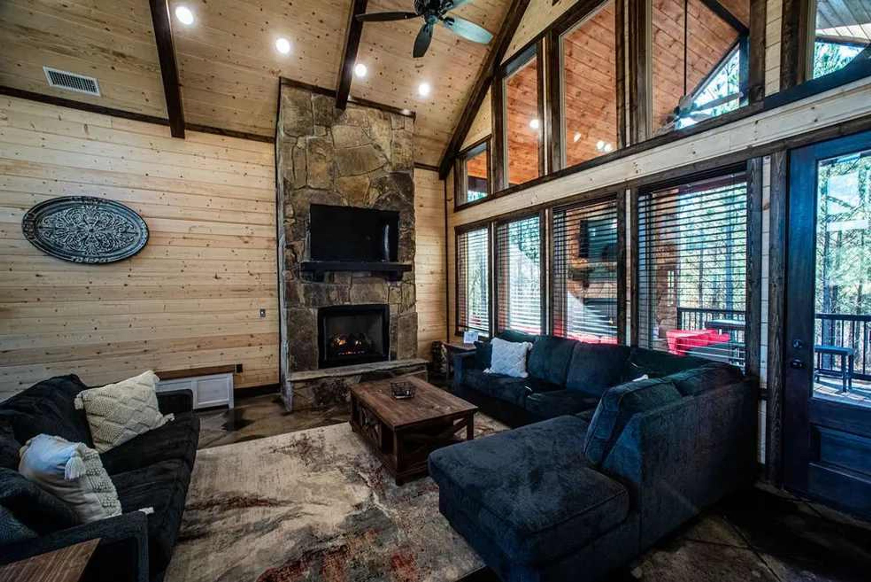 Un salon chaleureux avec une cheminée en pierre, des murs en bois et de grandes fenêtres.