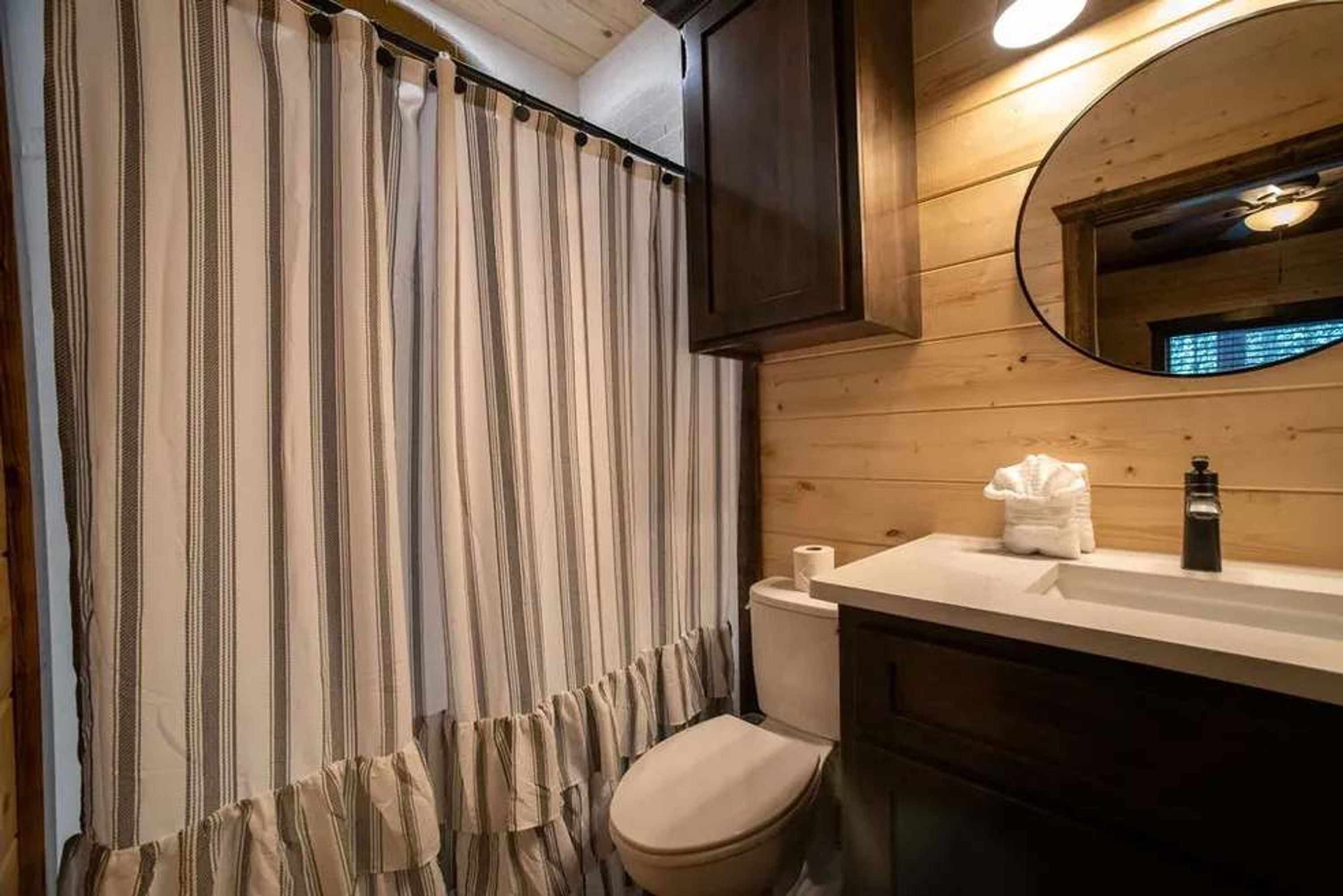 Une salle de bain avec un rideau à rayures, des toilettes, un lavabo avec une serviette et un miroir.