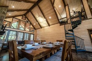 A spacious dining area with a high ceiling and wooden beams, a staircase, and large windows allowing natural light. - Sleeps 13 Hot Tub Arcade Firepit Games (Broken Bow)