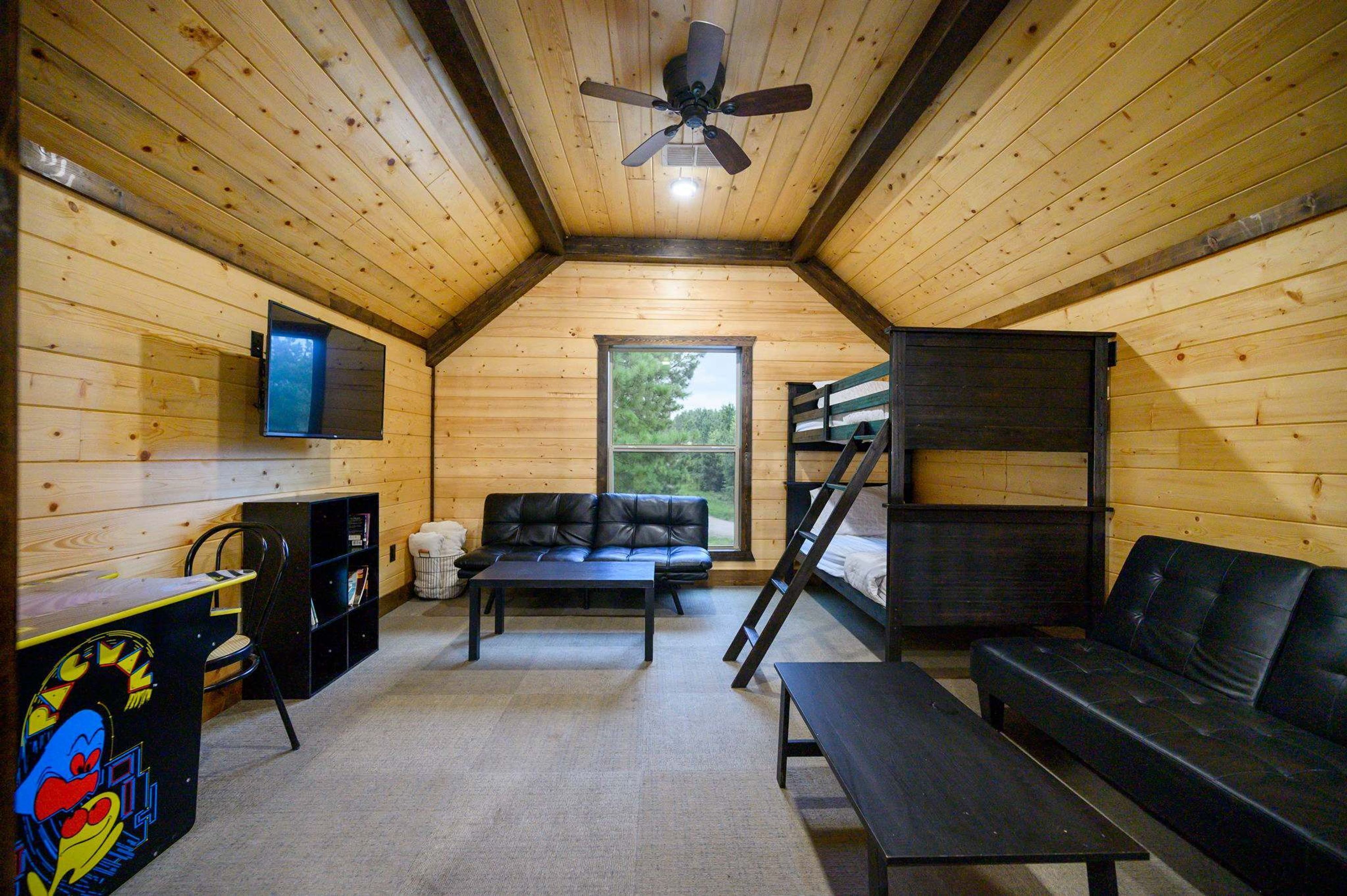 A cozy room with a ceiling fan, a TV mounted on the wall, a sofa, a coffee table, a bunk bed, and a bookshelf.