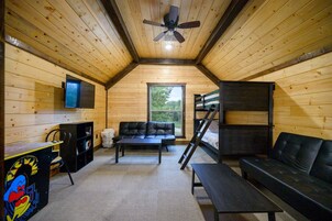 Una habitación acogedora con ventilador de techo, televisor montado en la pared, sofá, mesa de centro, litera y estantería.