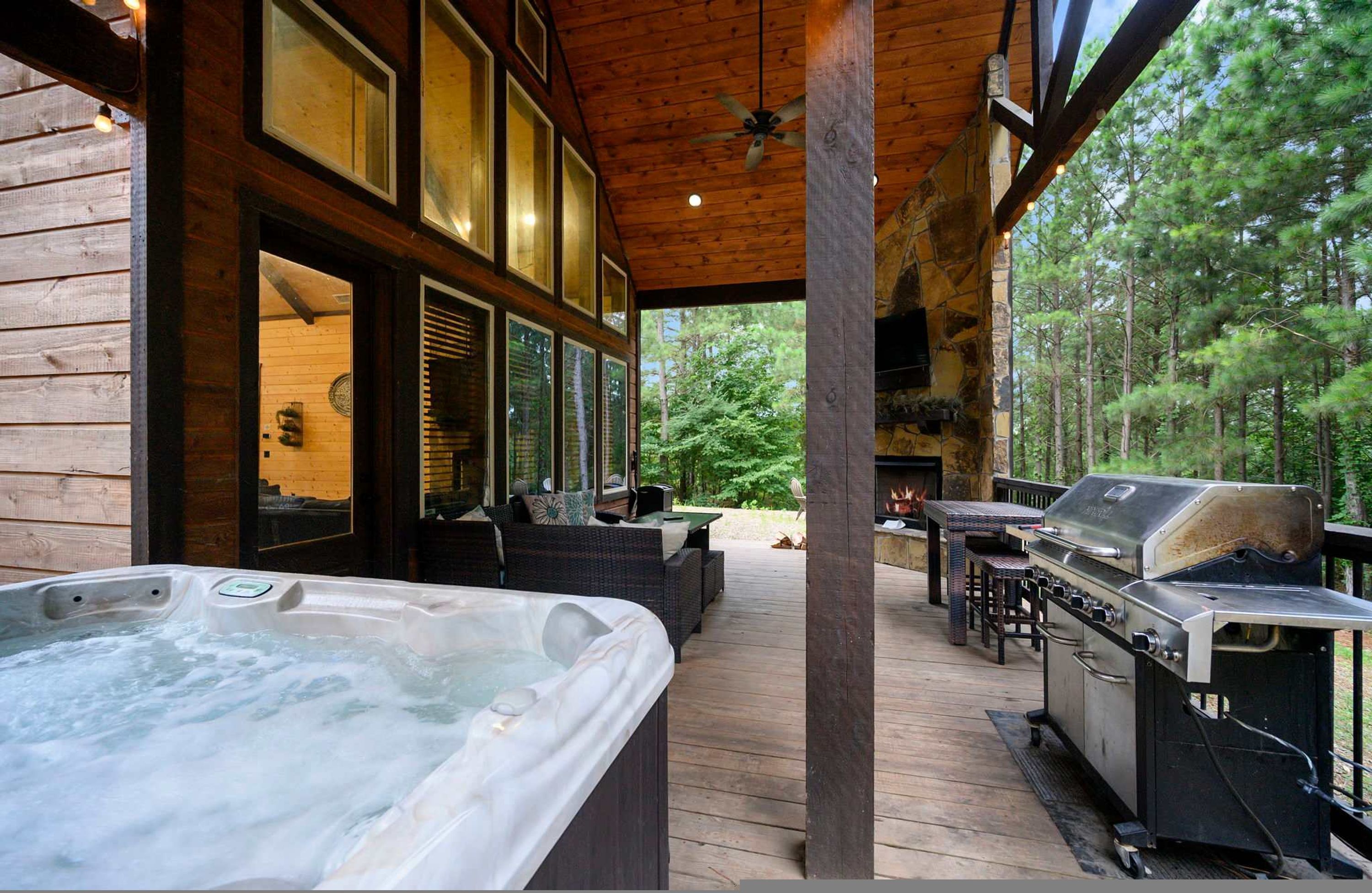 Eine Holzterrasse mit Whirlpool, Sitzgelegenheit im Freien und Grillbereich, umgeben von Bäumen.