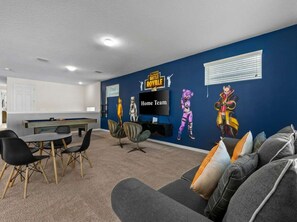 Um quarto com mesa de bilhar, cadeiras de jogos, um sofá com almofadas e uma parede com arte temática de jogos.