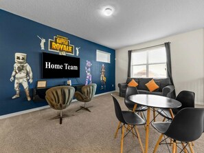 Quarto com parede azul decorativa, TV de tela plana, sofá e mesa de jantar com cadeiras.