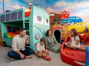 Eine Familie spielt in einem Bereich mit einem großen Spielzeugauto und einer farbenfrohen Wandmalerei.