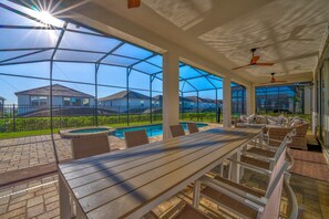 Eine überdachte Terrasse im Freien mit Pool, Sitzgelegenheiten und Blick auf Häuser im Hintergrund.