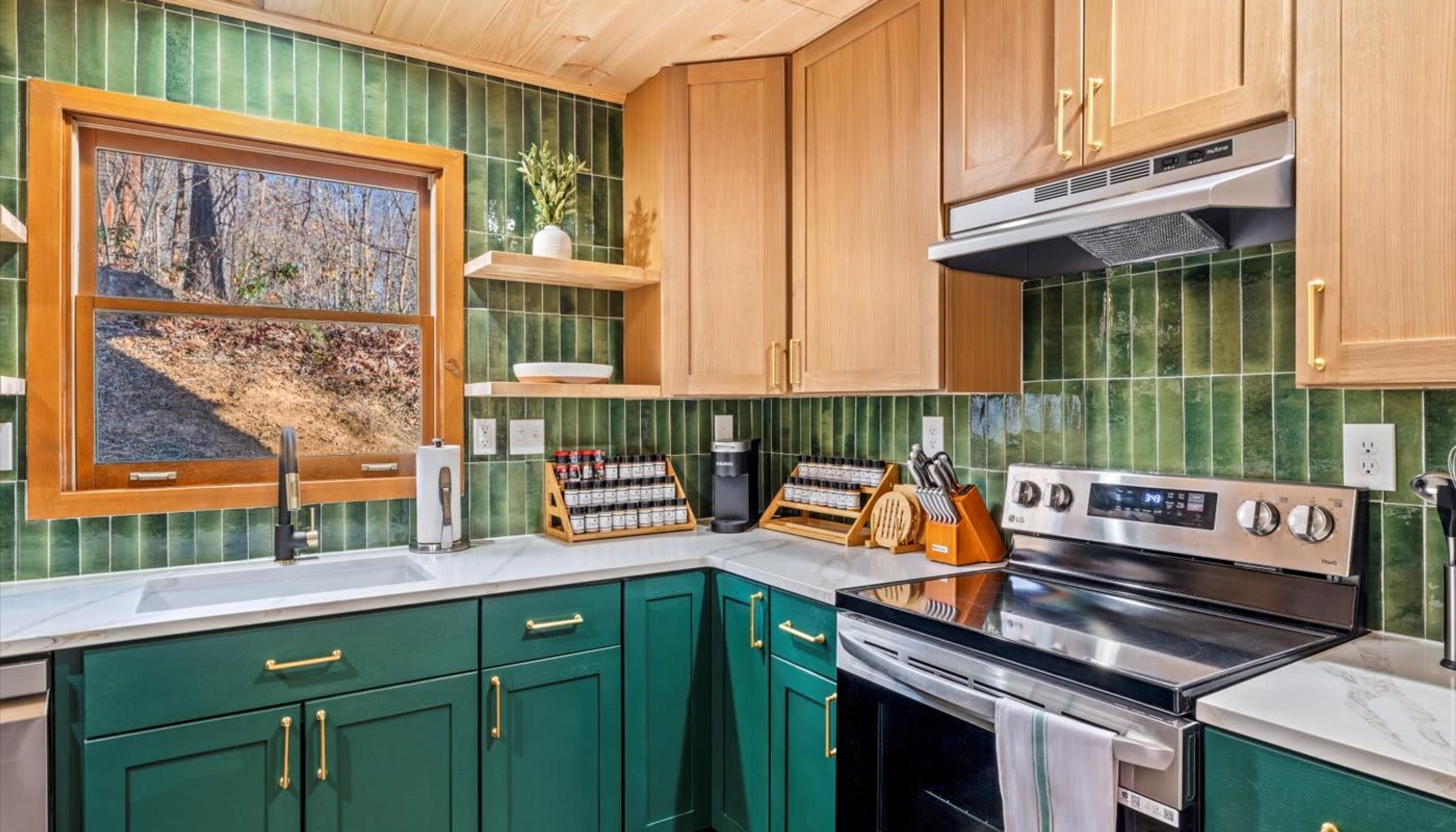 A kitchen with green cabinets, a stainless steel stove, and a window with a view of a forest.