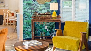 A room with a vibrant green leaf-patterned wall, a yellow armchair, a wooden side table with a book, and a window with blinds. - Sleeps 10 Pickleball Pool Tiki Bar Games (Bradenton)
