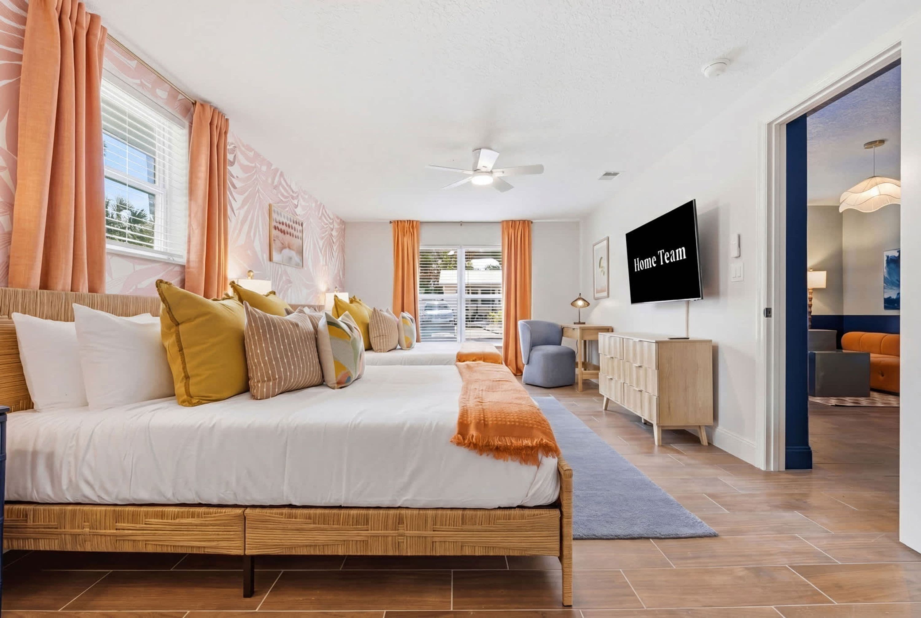 Un dormitorio moderno con cama, almohadas, televisor y ventilador de techo.